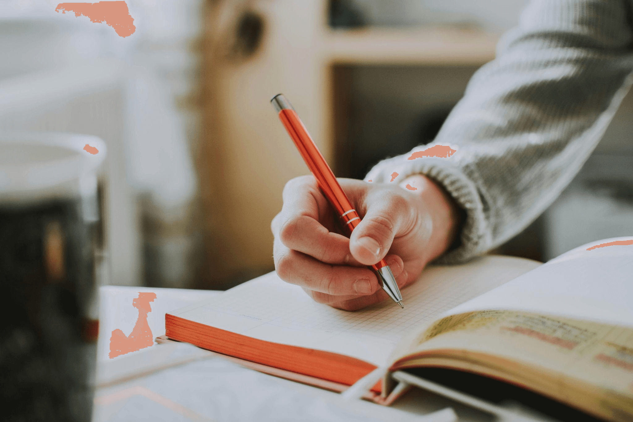 Close-up of a person holding an orange pen, writing in a notebook, representing professional book writers crafting compelling dialogue.