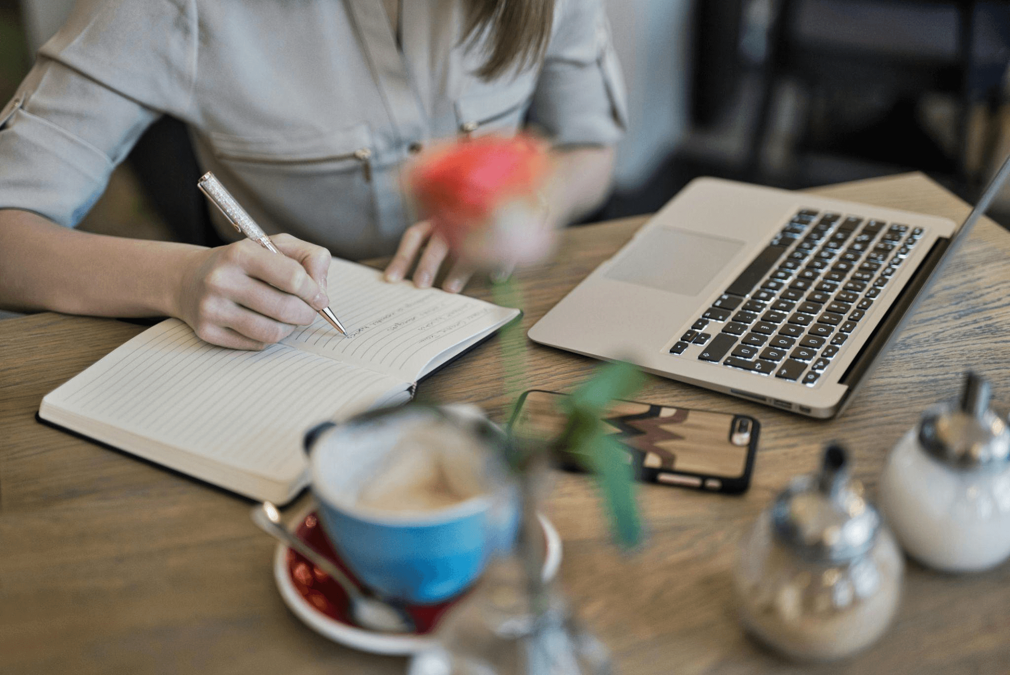 Person writing notes in a notebook beside an open MacBook, representing the process copywriting services follow.