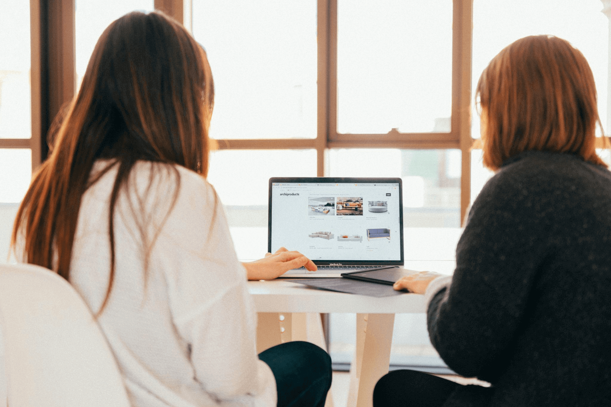 Two women discussing a web design project while looking at a laptop, collaborating with a web design agency.