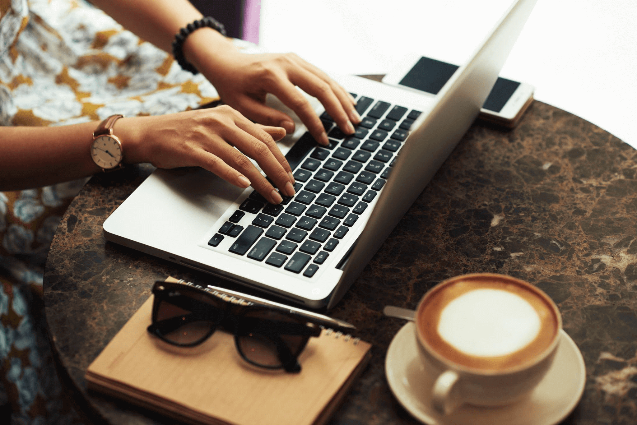 Person typing on a laptop in a café, symbolizing the process of writing SEO-friendly blog posts for semantic search optimization.