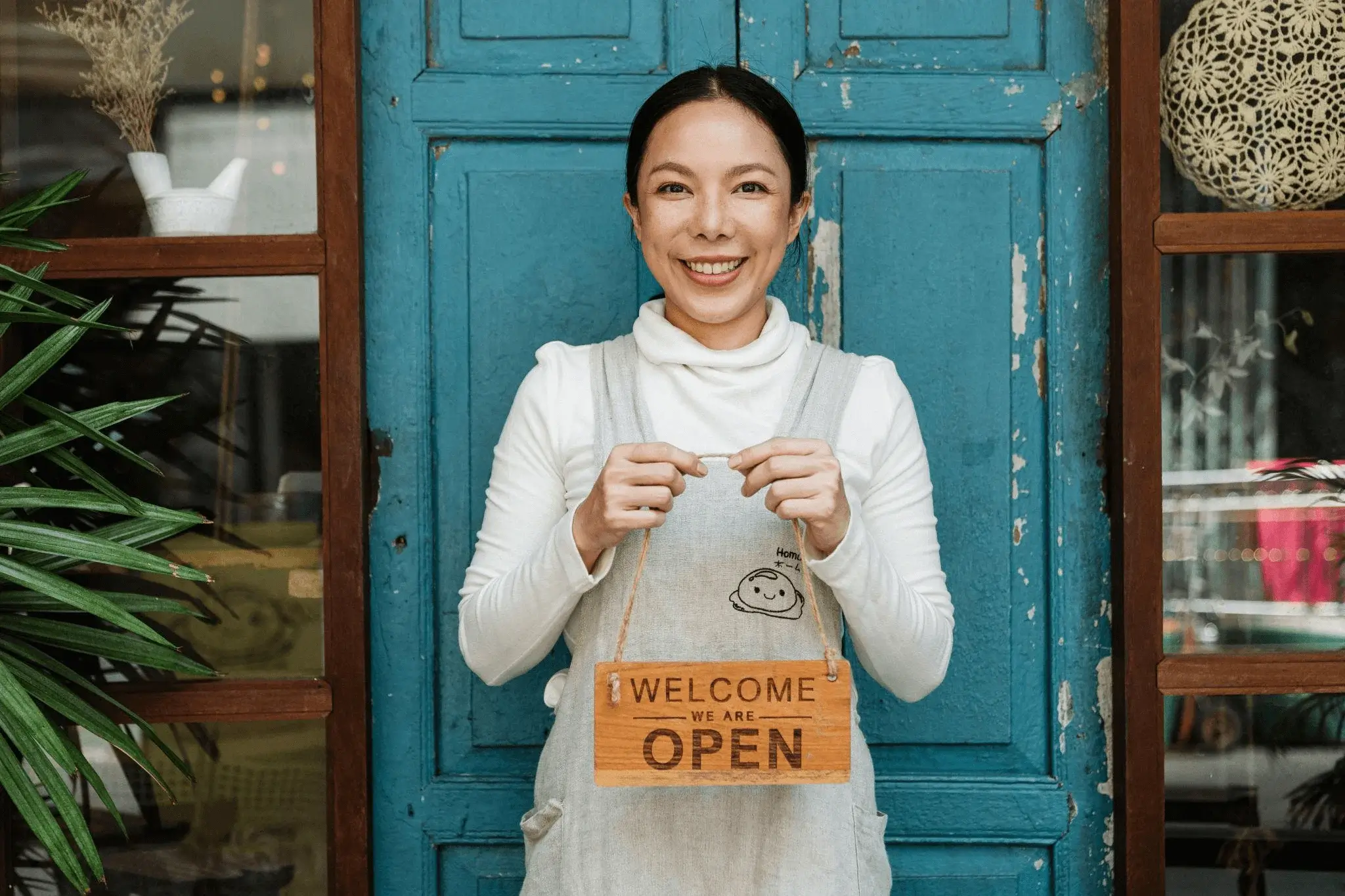 Smiling café owner holding a ‘We Are Open’ sign, representing how businesses generate organic visits for Google Business Profile by optimizing their local visibility and accurate listings.