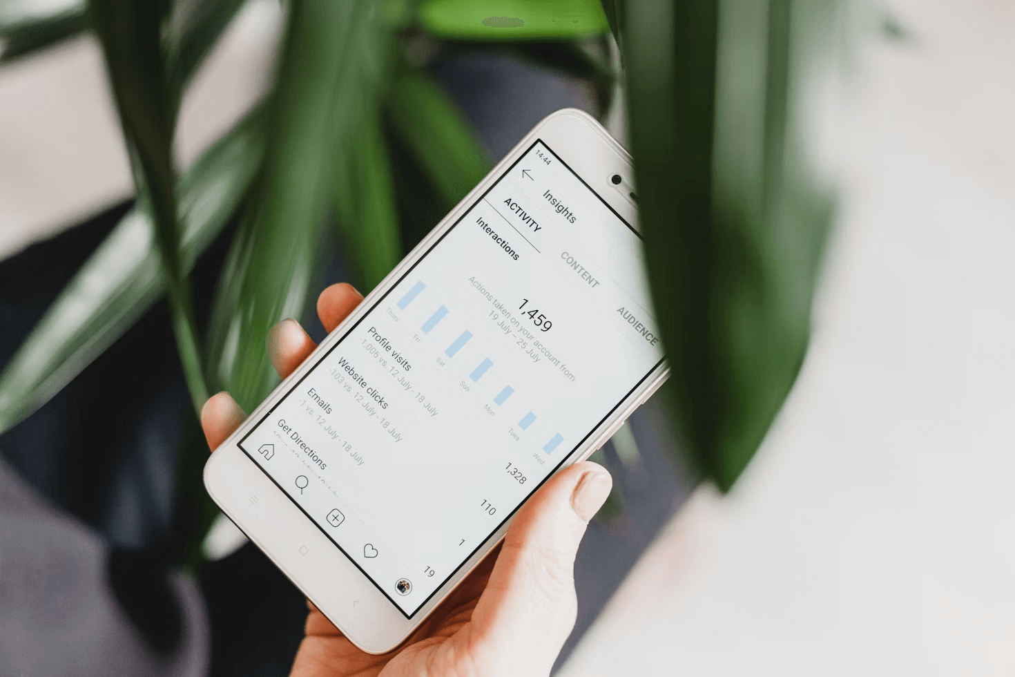 A person holding a smartphone displaying Instagram Insights analytics, showing profile visits, website clicks, and interactions data, which is useful for creating a strategy to get followers on Instagram.