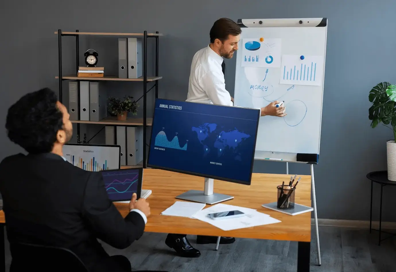 Two professionals in a modern office discuss data analytics and financial strategies, with one presenting charts and graphs on a whiteboard, illustrating a strategic meeting on implementing SEO for financial services.