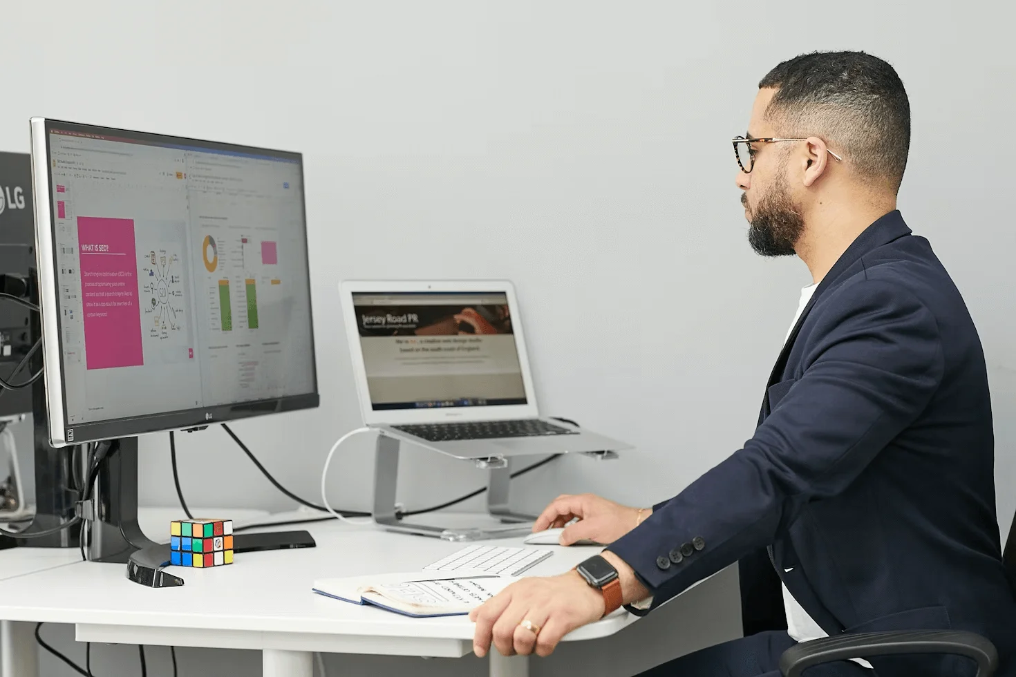 A digital marketing specialist sitting at a desk with a laptop and a computer, reflecting on why hiring a digital marketing agency is good for business growth and online success.