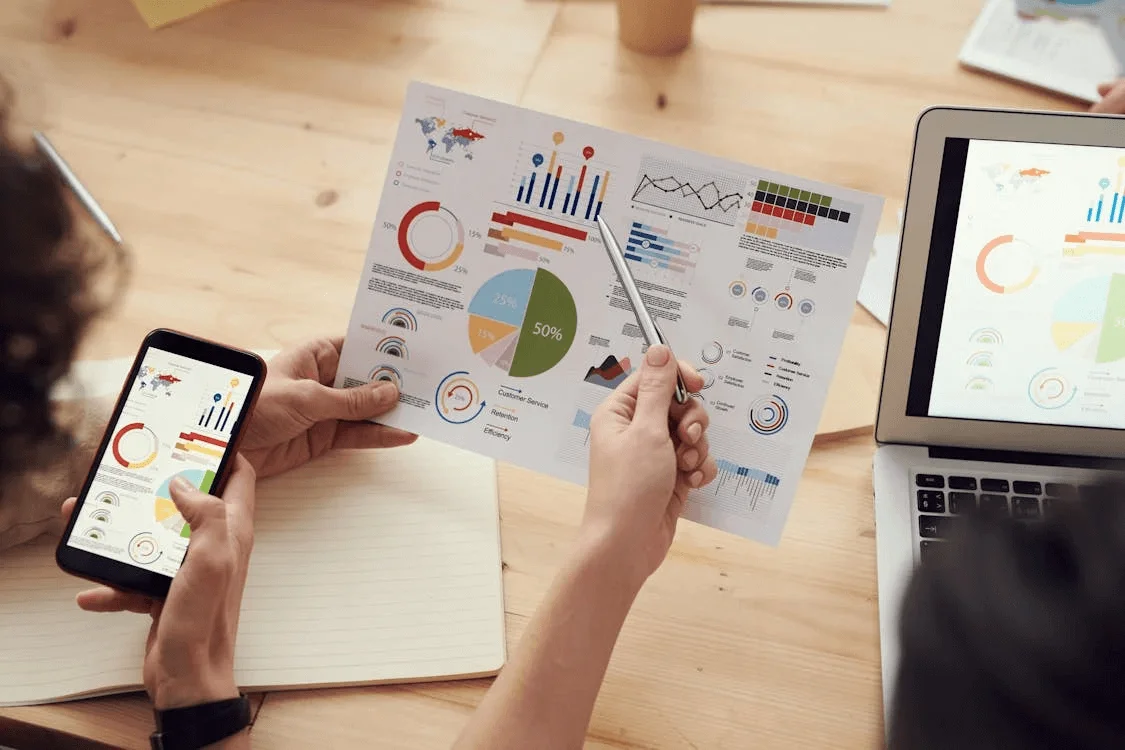 Team analyzing marketing performance charts on paper, laptop, and phone, illustrating data-driven decisions and highlighting why hire a digital marketing agency for measurable results.